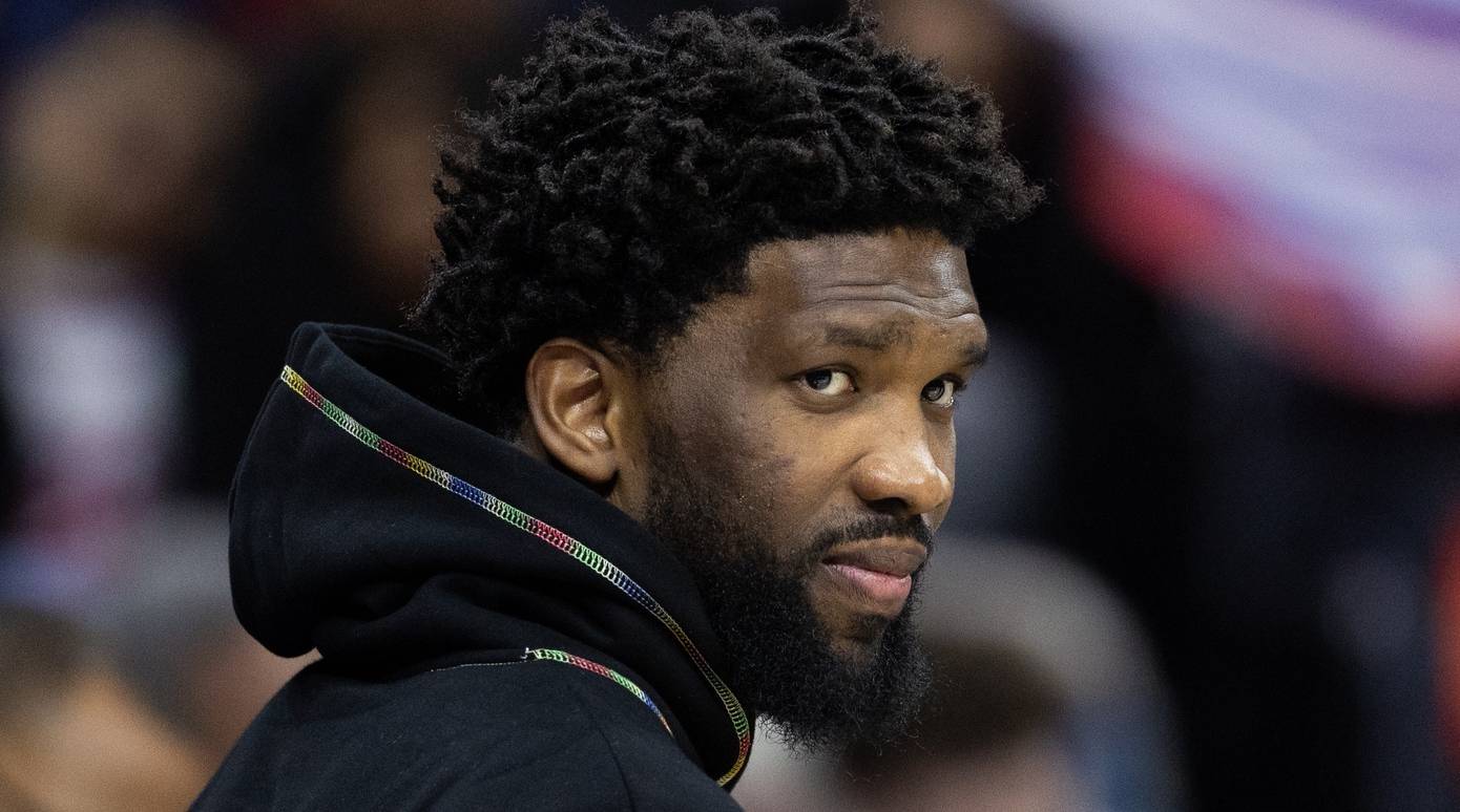 76ers center Joel Embiid looks on in street clothes during a game.